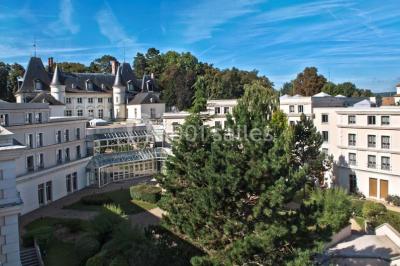Vue aérienne d'un bâtiment en forme de cour rectangulaire avec des toits en tuiles, entouré de champs et d'arbres.