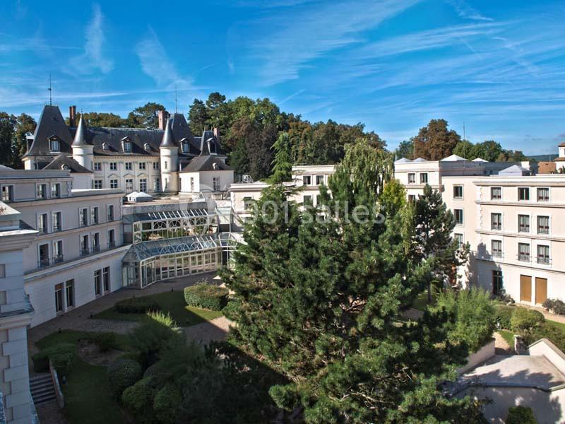 Vue aérienne d'un bâtiment élégant entouré de jardins arborés sous un ciel bleu dégagé.