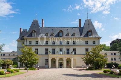 Vue aérienne d'un bâtiment en forme de cour rectangulaire avec des toits en tuiles, entouré de champs et d'arbres.