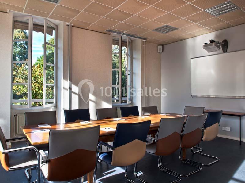 Salle de réunion lumineuse avec une grande table en bois, des chaises modernes et un tableau blanc au mur.