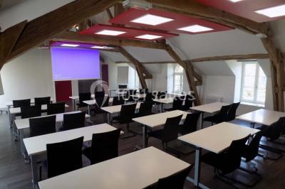Vue aérienne d'un bâtiment en forme de cour rectangulaire avec des toits en tuiles, entouré de champs et d'arbres.
