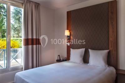 Vue aérienne d'un bâtiment en forme de cour rectangulaire avec des toits en tuiles, entouré de champs et d'arbres.