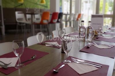 Vue aérienne d'un bâtiment en forme de cour rectangulaire avec des toits en tuiles, entouré de champs et d'arbres.