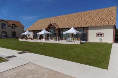 Vue aérienne d'un bâtiment en forme de cour rectangulaire avec des toits en tuiles, entouré de champs et d'arbres.