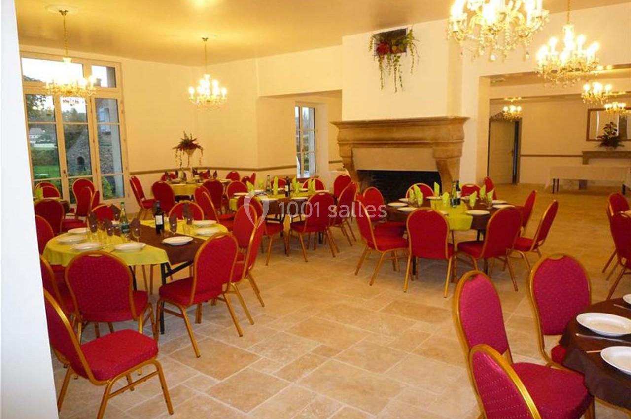 Salle de réception lumineuse avec tables dressées, chaises rouges et lustres suspendus.