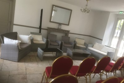 Mobilier de jardin en rotin avec coussins, disposé dans une véranda lumineuse avec des plantes en pot.