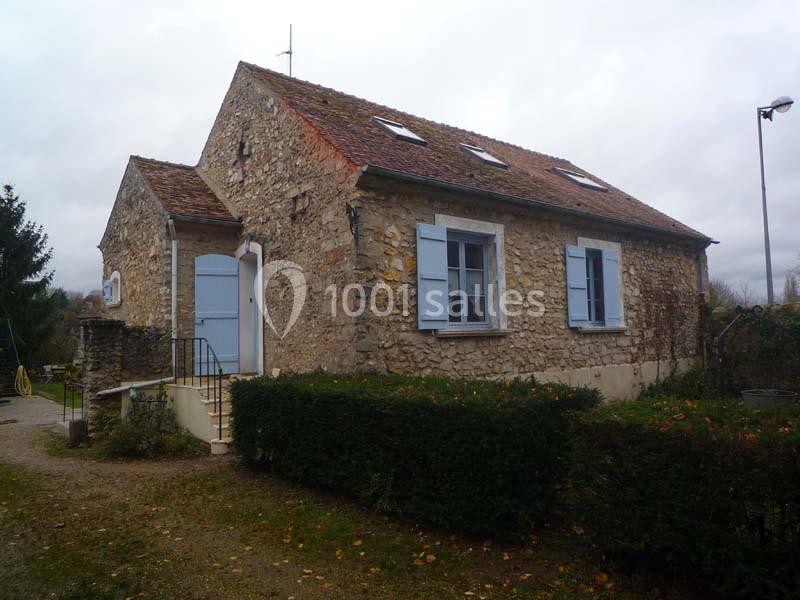 Maison en pierre avec volets bleus, toit en tuiles et jardin, sous un ciel nuageux.