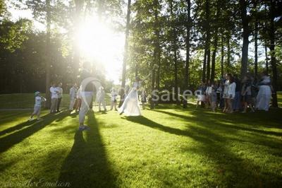 Maison en bois éclairée la nuit, entourée d'arbres illuminés, sous un ciel nuageux avec la lune visible.