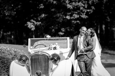 Maison en bois éclairée la nuit, entourée d'arbres illuminés, sous un ciel nuageux avec la lune visible.