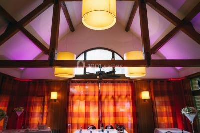 Maison en bois éclairée la nuit, entourée d'arbres illuminés, sous un ciel nuageux avec la lune visible.