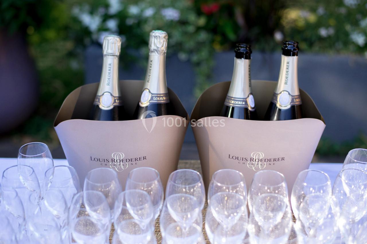Bouteilles de champagne Louis Roederer dans des seaux en carton beige, entourées de verres vides sur une table.
