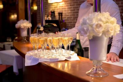 Maison en bois éclairée la nuit, entourée d'arbres illuminés, sous un ciel nuageux avec la lune visible.