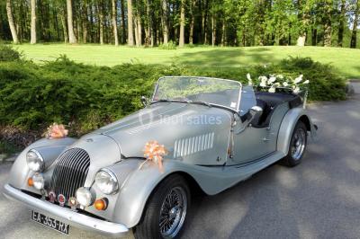 Maison en bois éclairée la nuit, entourée d'arbres illuminés, sous un ciel nuageux avec la lune visible.