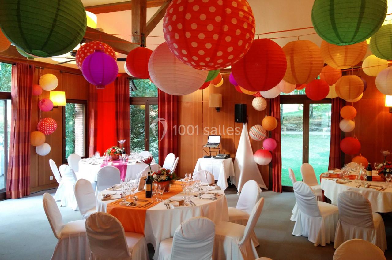 Salle décorée pour un événement avec des lanternes colorées suspendues et des tables dressées avec nappes blanches.