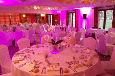 Maison en bois éclairée la nuit, entourée d'arbres illuminés, sous un ciel nuageux avec la lune visible.