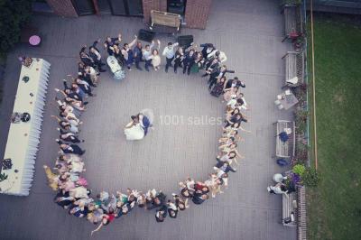 Maison en bois éclairée la nuit, entourée d'arbres illuminés, sous un ciel nuageux avec la lune visible.