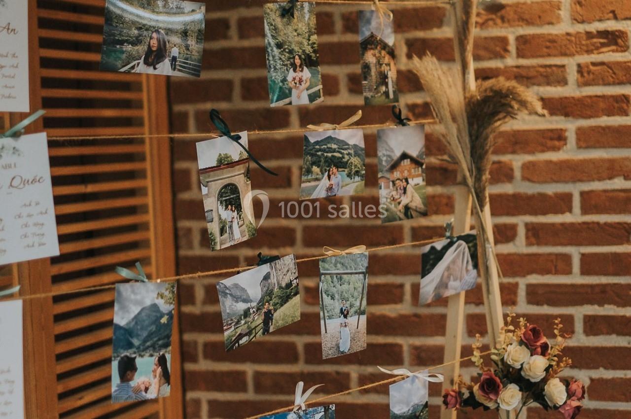 Photos accrochées à une structure en bois décorée de feuillage et de fleurs, devant un mur en briques.