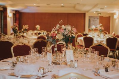 Maison en bois éclairée la nuit, entourée d'arbres illuminés, sous un ciel nuageux avec la lune visible.