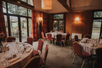Maison en bois éclairée la nuit, entourée d'arbres illuminés, sous un ciel nuageux avec la lune visible.