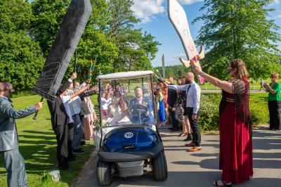 Maison en bois éclairée la nuit, entourée d'arbres illuminés, sous un ciel nuageux avec la lune visible.