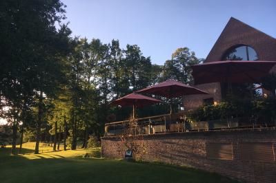 Maison en bois éclairée la nuit, entourée d'arbres illuminés, sous un ciel nuageux avec la lune visible.