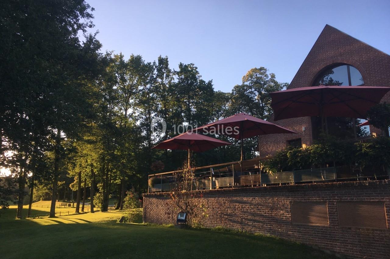Terrasse en briques avec parasols rouges, entourée d'arbres et d'une pelouse, éclairée par une lumière de fin de journée.