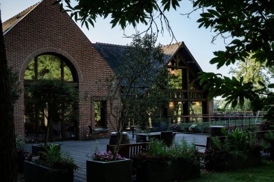 Maison en bois éclairée la nuit, entourée d'arbres illuminés, sous un ciel nuageux avec la lune visible.