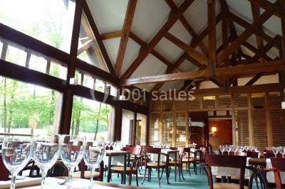 Maison en bois éclairée la nuit, entourée d'arbres illuminés, sous un ciel nuageux avec la lune visible.