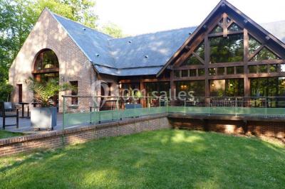 Maison en bois éclairée la nuit, entourée d'arbres illuminés, sous un ciel nuageux avec la lune visible.