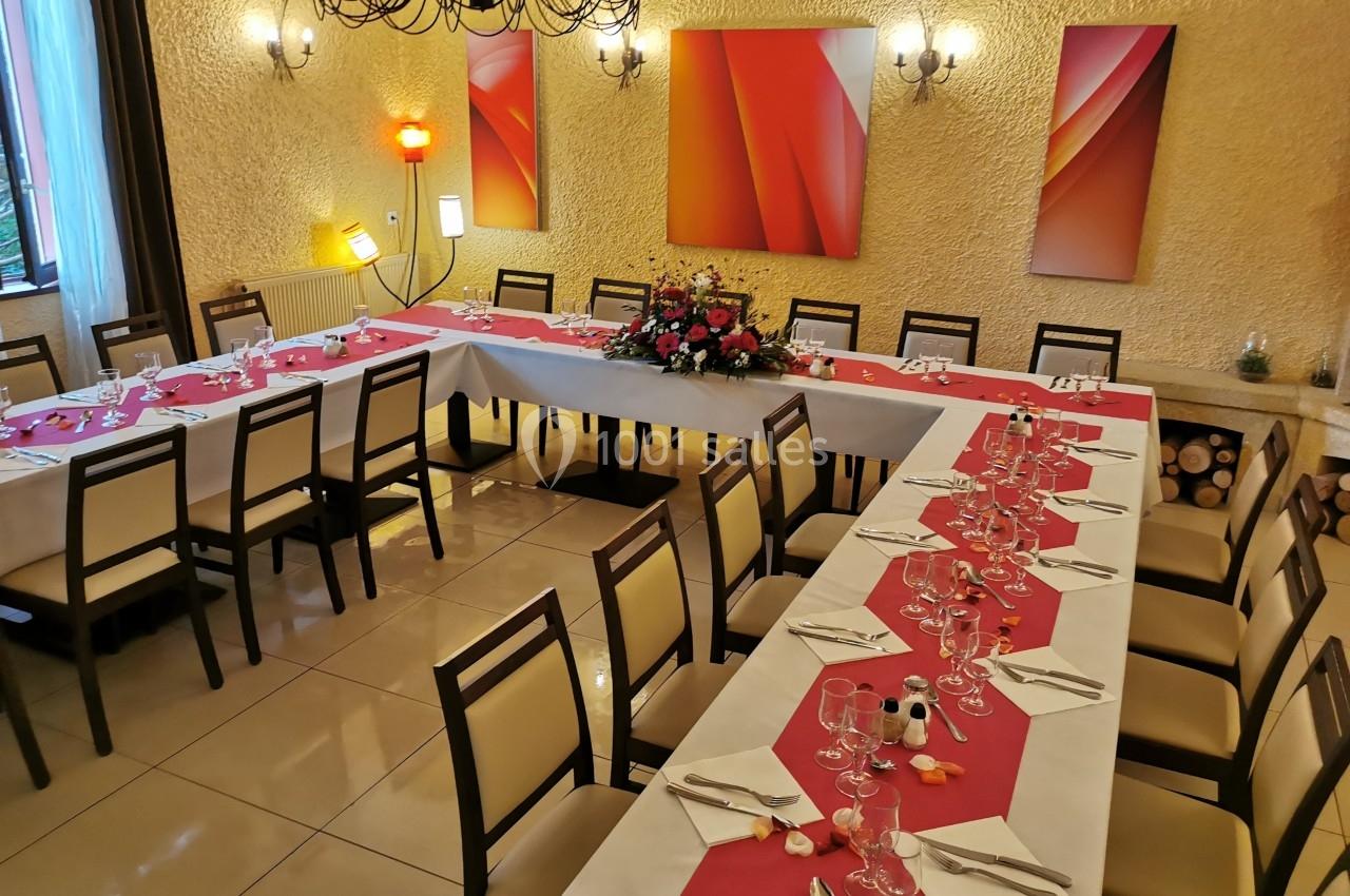 Salle de réception avec tables dressées en U, nappes blanches et chemins de table rouges, décorations florales au centre.