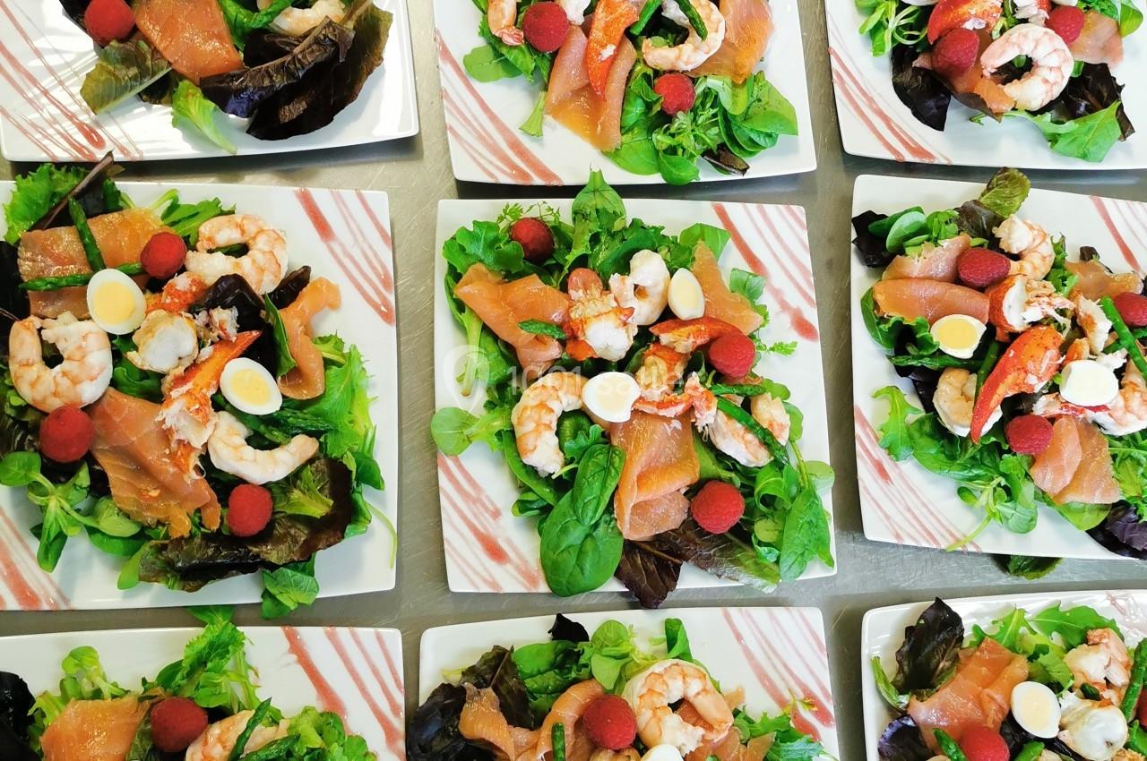 Assiettes de salades composées avec crevettes, saumon fumé, œufs de caille, framboises et feuilles vertes.