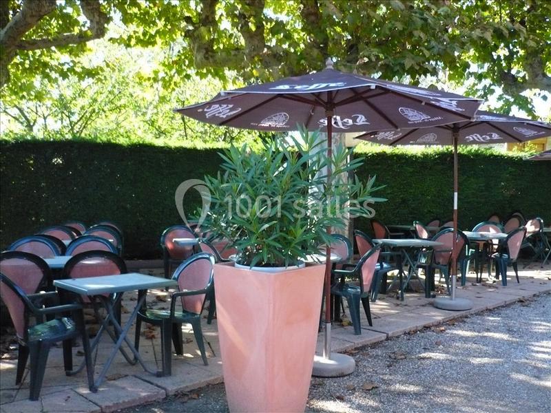 Terrasse extérieure avec des tables et chaises vides sous des parasols, entourée de verdure et d'arbres.