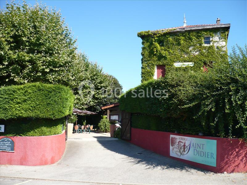 Entrée d'une auberge entourée de verdure, avec une terrasse ombragée et un bâtiment recouvert de lierre.