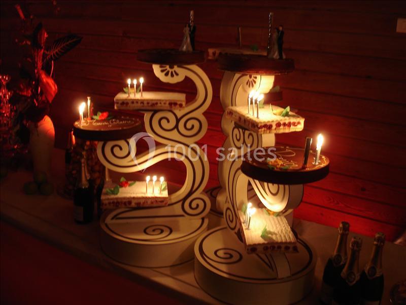 Présentoir décoratif illuminé avec des gâteaux de mariage et des bougies, entouré de bouteilles et d'éléments décoratifs.