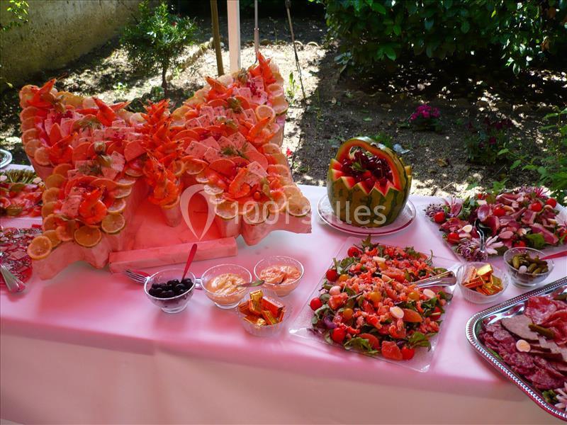 Buffet coloré avec sculptures de fruits, salades variées et décorations sur une table en extérieur.