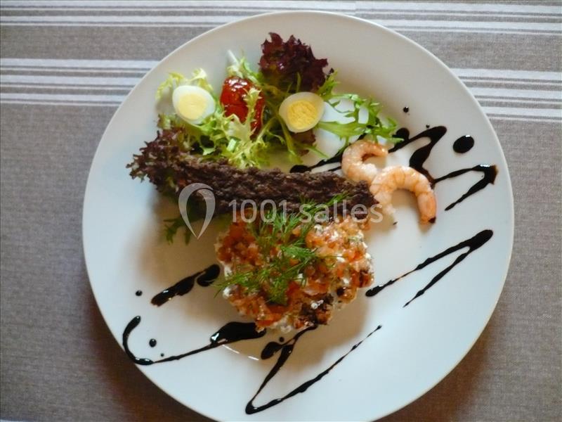 Assiette composée de tartare de saumon, crevette, salade verte et décorations de sauce balsamique.