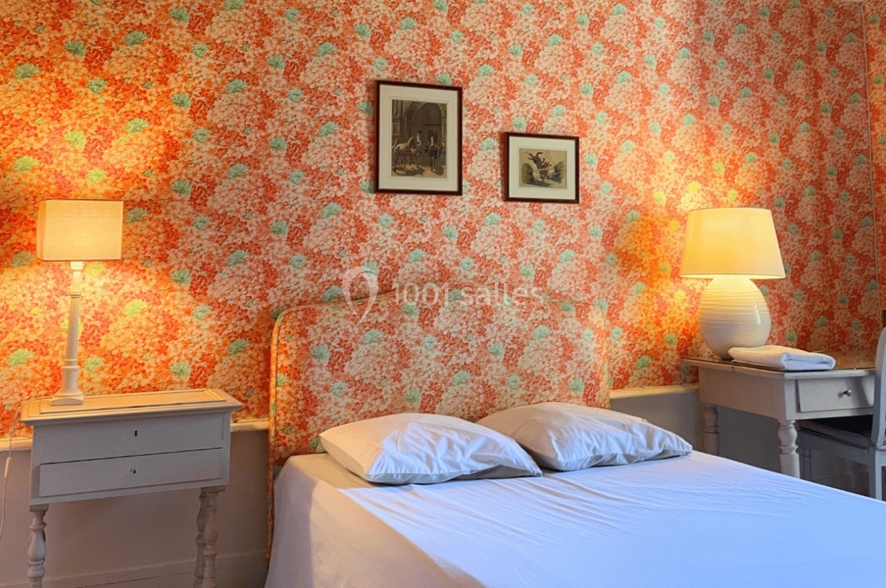 Chambre avec lit double, murs tapissés de motifs floraux colorés, deux lampes de chevet et cadres décoratifs.