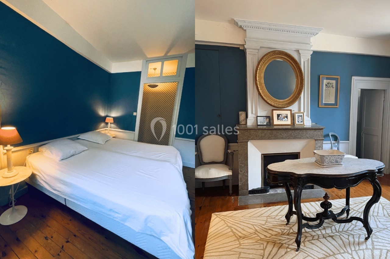 Chambre avec murs bleus, lit double, table basse, cheminée décorative et miroir doré dans un intérieur lumineux.