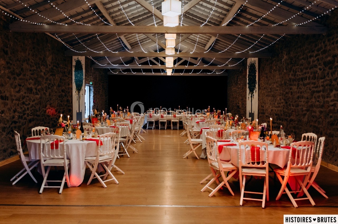 Salle de réception décorée avec des tables rondes, nappes blanches, chaises blanches et éclairage chaleureux.