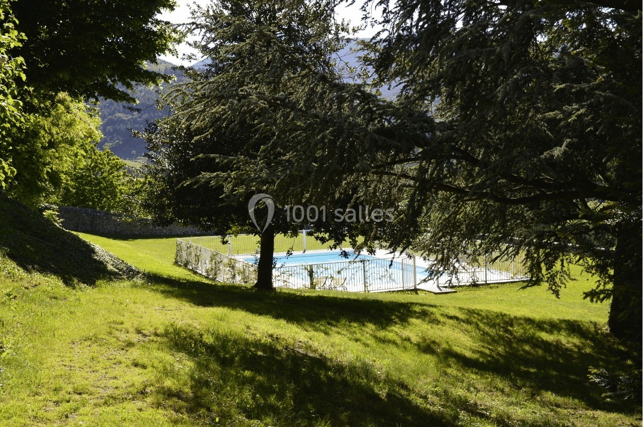 Piscine extérieure entourée de pelouse et d'arbres, avec des collines visibles en arrière-plan.