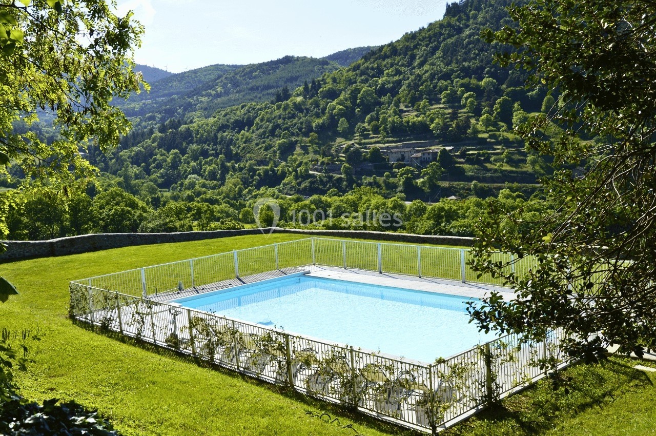 Piscine extérieure clôturée entourée de pelouse, avec vue sur des collines verdoyantes et un ciel dégagé.