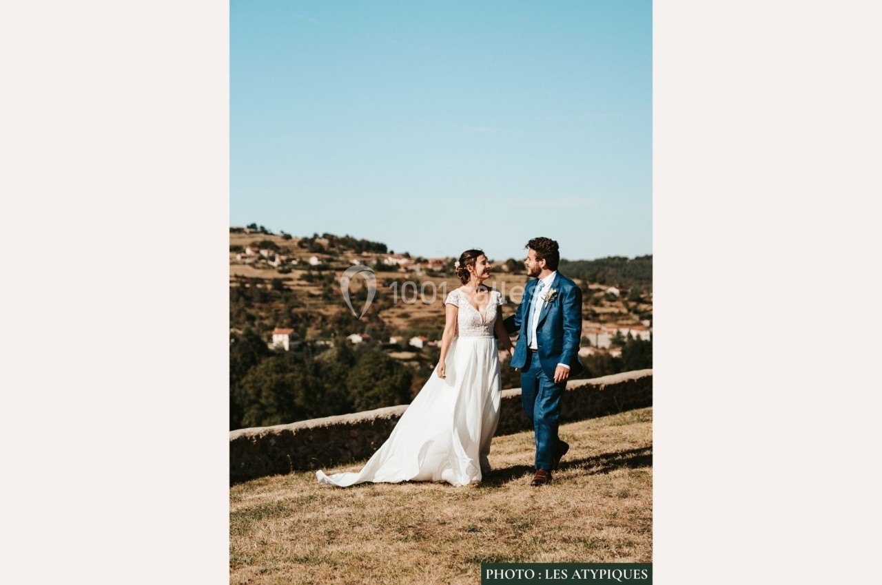 Un couple en tenue de mariage marche sur une pelouse avec un paysage vallonné en arrière-plan.
