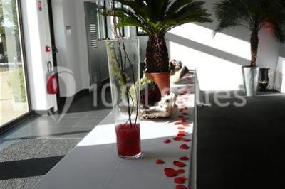 Table décorée avec un vase, des pétales rouges et des plantes en pot dans une salle lumineuse.