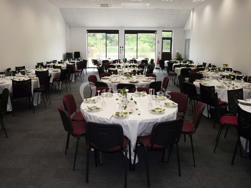 Salle de réception aménagée avec des tables rondes dressées pour un événement, vue sur des baies vitrées donnant sur l…