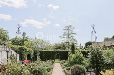 Serre illuminée au crépuscule, entourée de murs en pierre et d'arbres, avec une tour en arrière-plan.