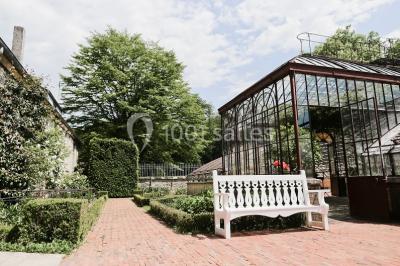 Serre illuminée au crépuscule, entourée de murs en pierre et d'arbres, avec une tour en arrière-plan.