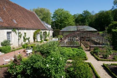 Serre illuminée au crépuscule, entourée de murs en pierre et d'arbres, avec une tour en arrière-plan.
