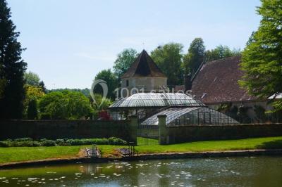 Serre illuminée au crépuscule, entourée de murs en pierre et d'arbres, avec une tour en arrière-plan.