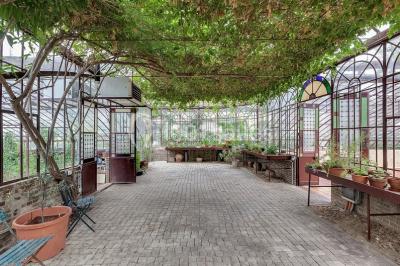 Serre illuminée au crépuscule, entourée de murs en pierre et d'arbres, avec une tour en arrière-plan.