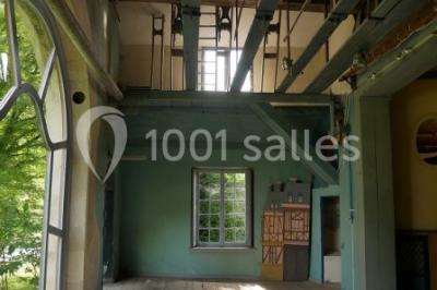 Serre illuminée au crépuscule, entourée de murs en pierre et d'arbres, avec une tour en arrière-plan.